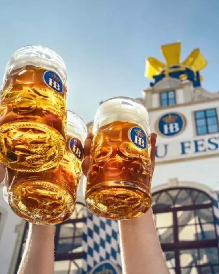 Two full beer steins raised in front of a Bavarian festival tent